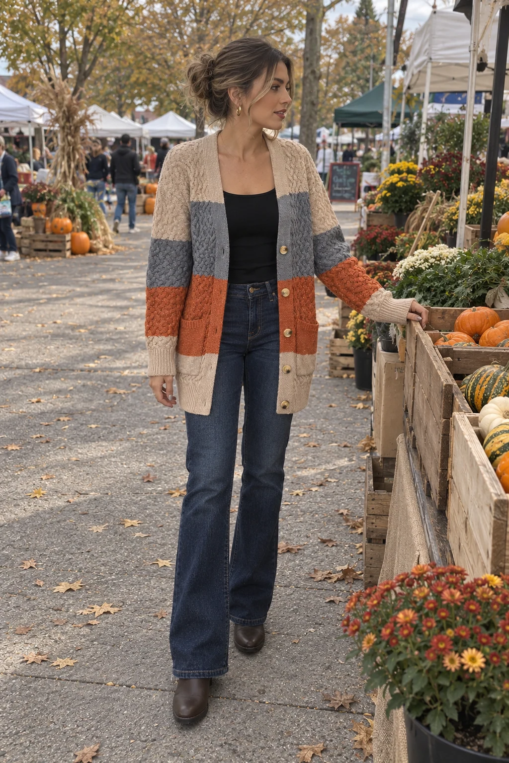 A woman browsing an outdoor autumn market in a beige, grey and rust colorblock cable cardigan, dark bootcut jeans and brown boots